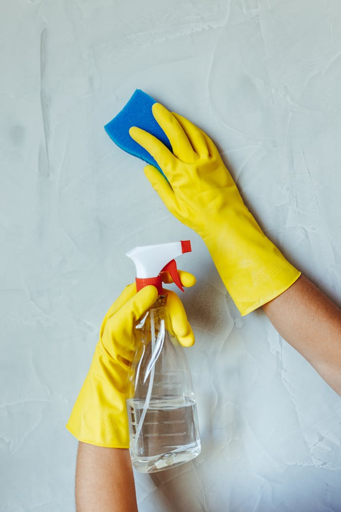 hero-img-02 Hands in yellow gloves cleaning wall with sponge and spray bottle.